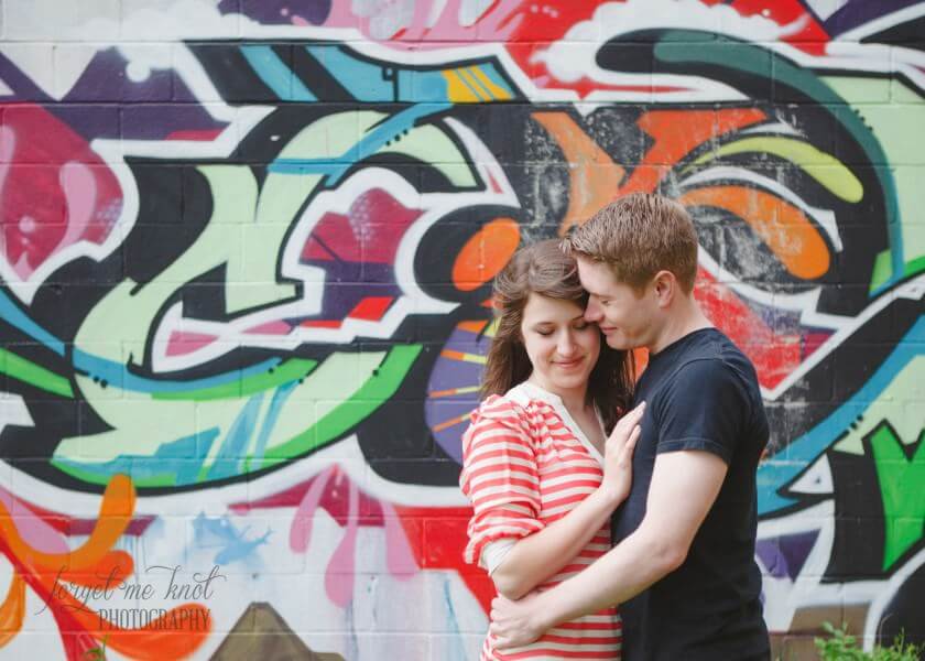 engaged couple snuggling by graffiti wall