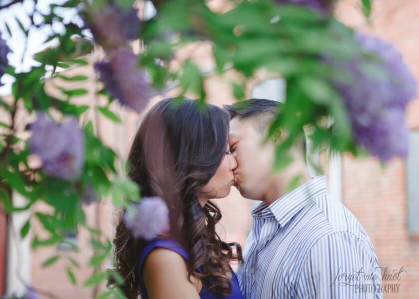engaged couple kissing on other side of purple flowers
