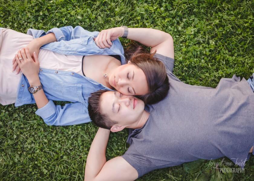 engaged couple with eyes closed while laying in grass at park