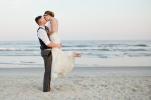 groom holding bride up while kissing on ocean isle beach