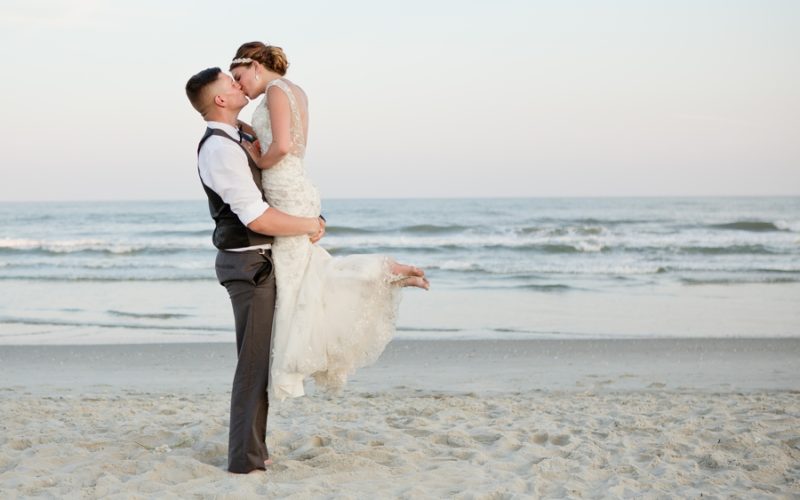 groom holding bride up while kissing on ocean isle beach