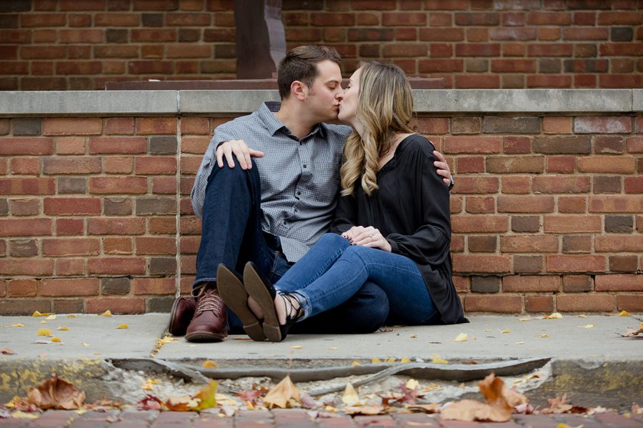 engaged couple kissing while sitting on sidewalk