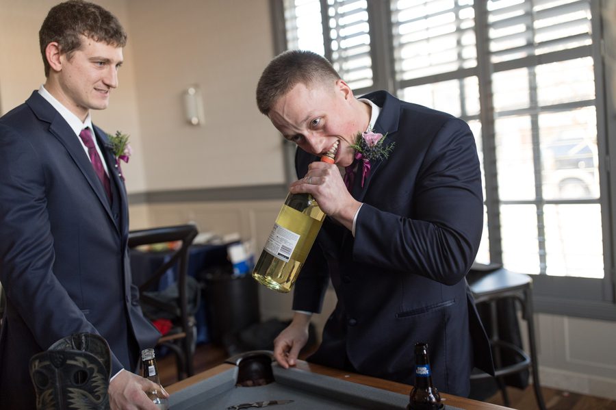 groomsmen opening wine bottle with teeth