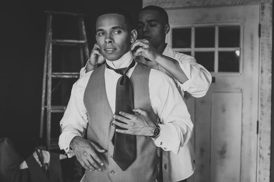 black and white photo of groom getting tie on