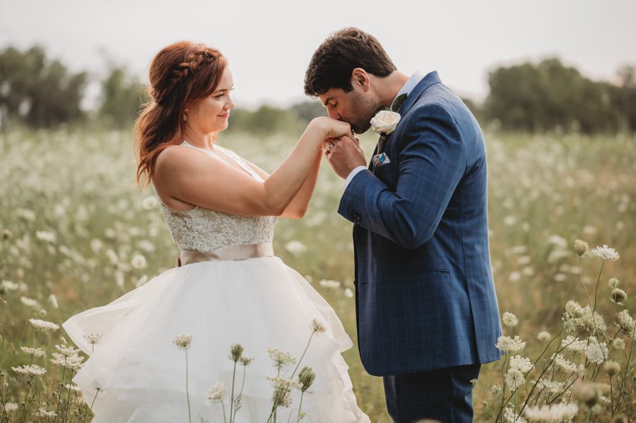 groom kissing brides hand in flower field at Brookshire Event Center