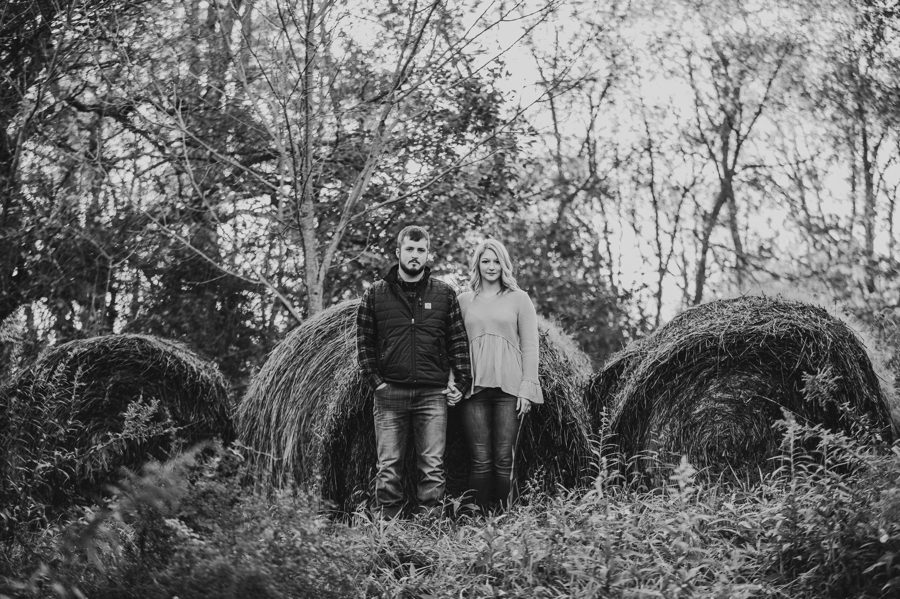 black and white image of engaged couple not smiling in front of hay bails at Camping Engagement Photos in Mount Vernon Ohio