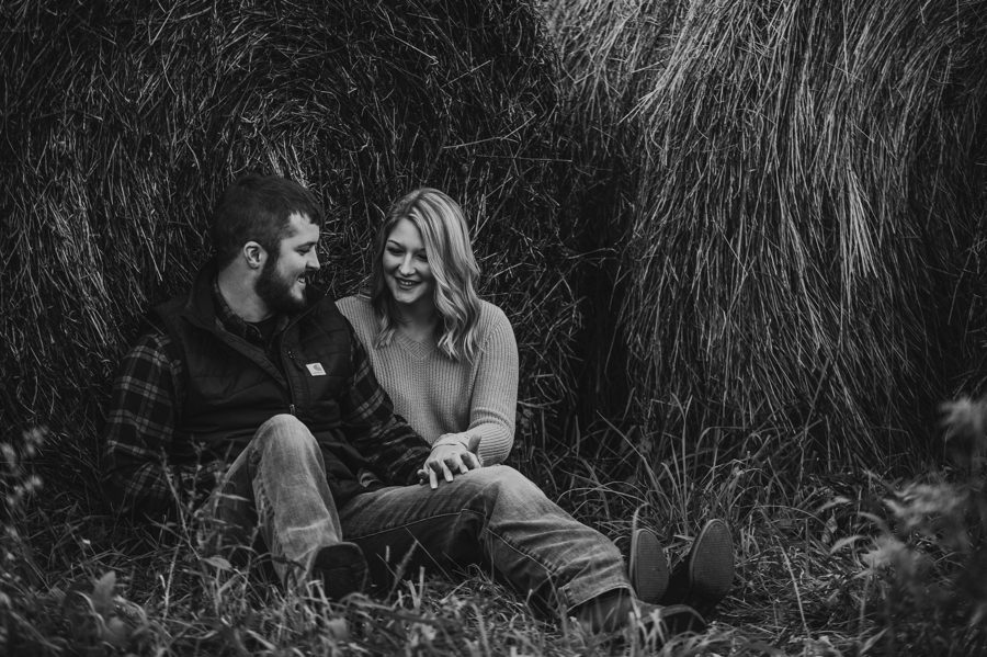 black and white image of couple sitting against hay bales holding hands in Mount Vernon Ohio