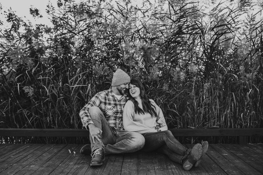 black and white image of engaged couple sitting on dock laughing for Engagement Photos at Grange Audubon