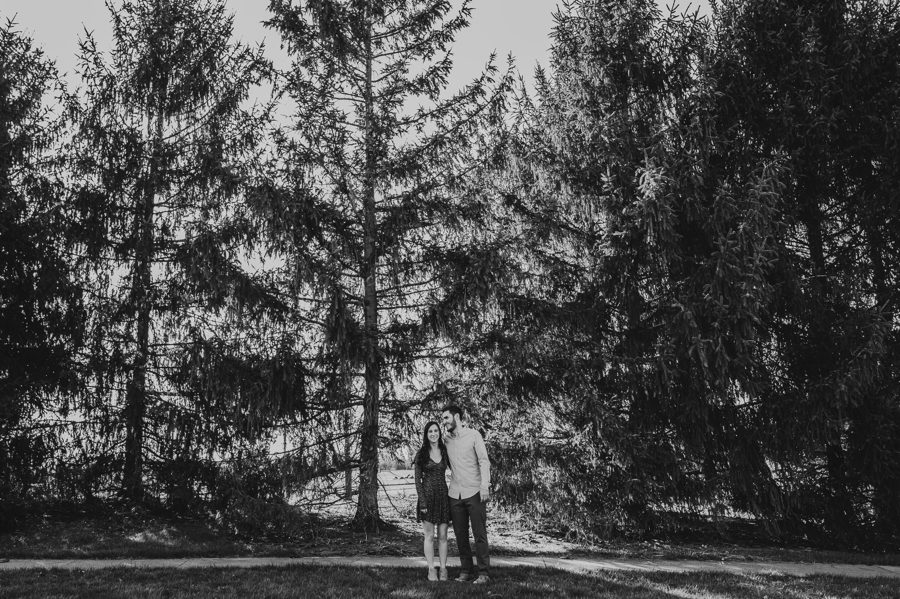 black and white image of engaged couple laughing with large pine trees