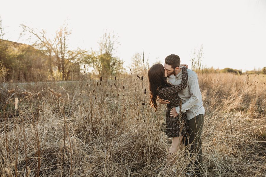 engaged couple kissing while standing in field with cattails