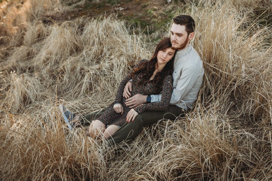 engaged couple sitting in field cuddled together