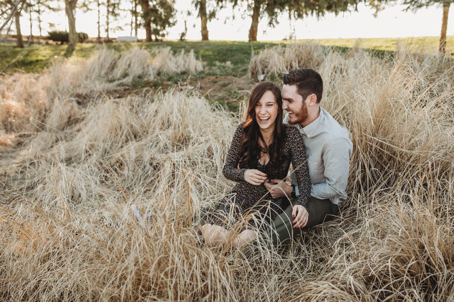 engaged couple laughing while sitting in field at Homestead Park Engagement