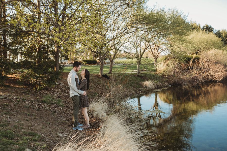 engaged couple standing near pond looking at each other
