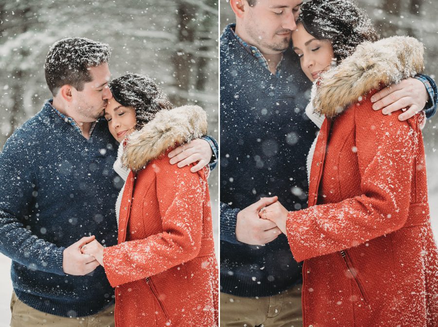 man kissing fiancés head with red coat in the snow