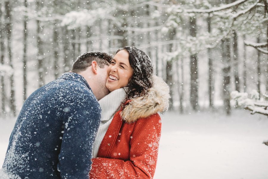 man blowing raspberries on fiancés neck at tall pines in the snow at Hoover Reservoir Engagement