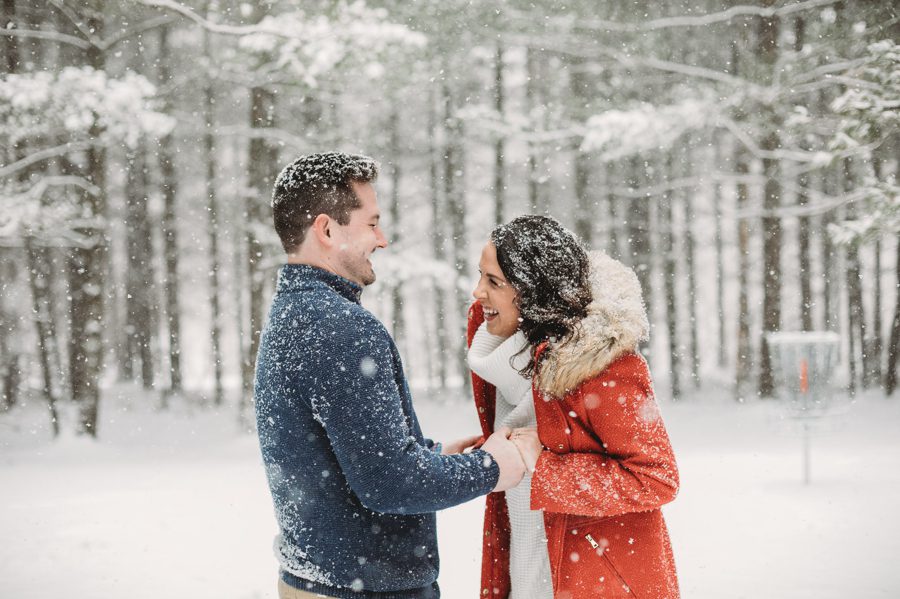 candid image of engaged couple laughing in the snow with tall pines