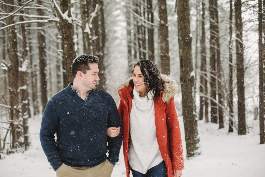 engaged couple laughing while walking in the snow