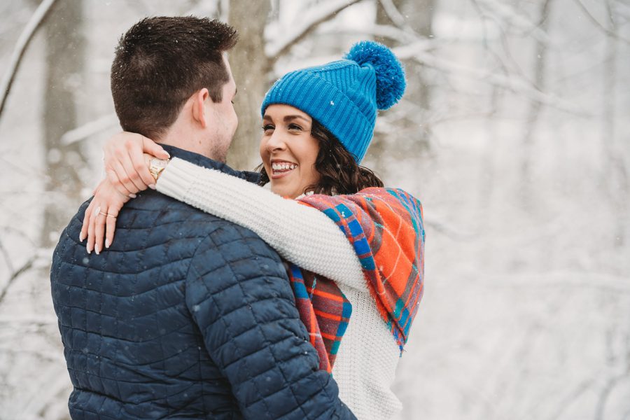 woman in blue at in the snow with arms wrapped around fiancés neck