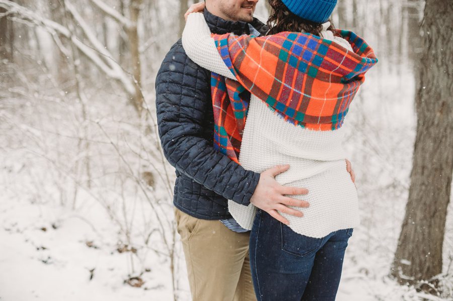 man with hands wrapped around fiancés hips at snowy engagement session