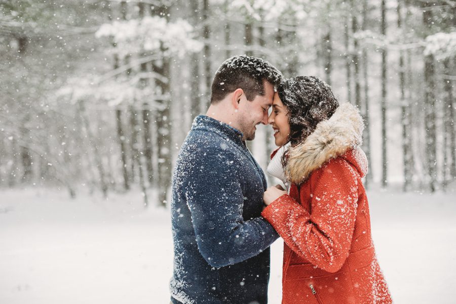 engaged couple with foreheads together with snowy tall pines