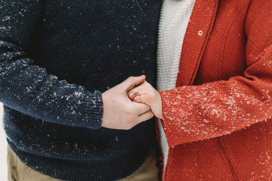 close up image of engaged couple holding hands in the snow