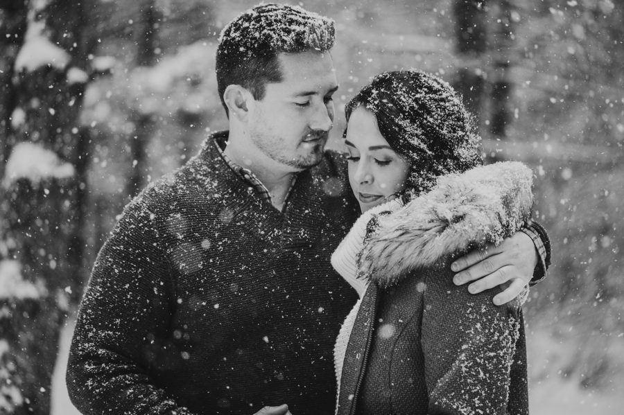 black and white image of man with his arm around fiancé in the snow