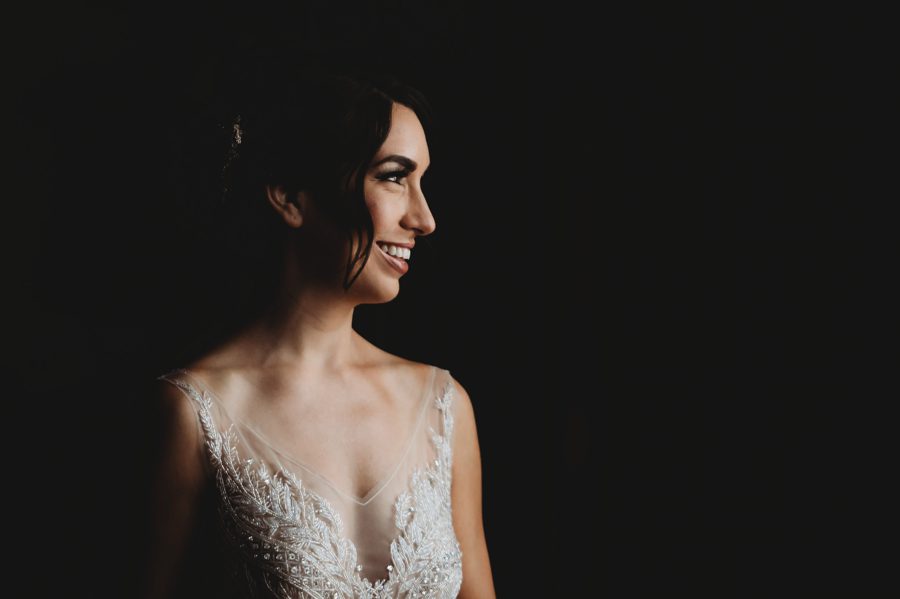 moody photo of bride looking out window smiling