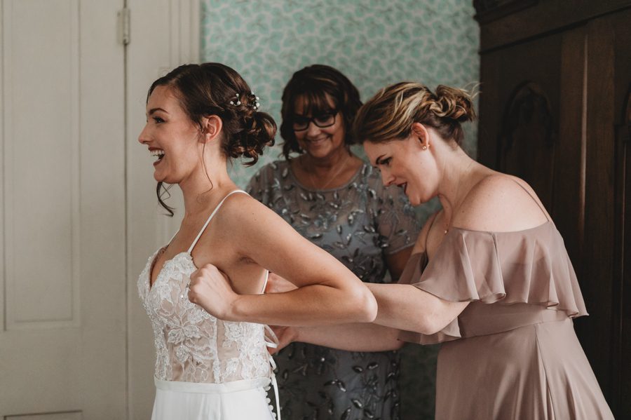 bride laughing as her dress is being put on