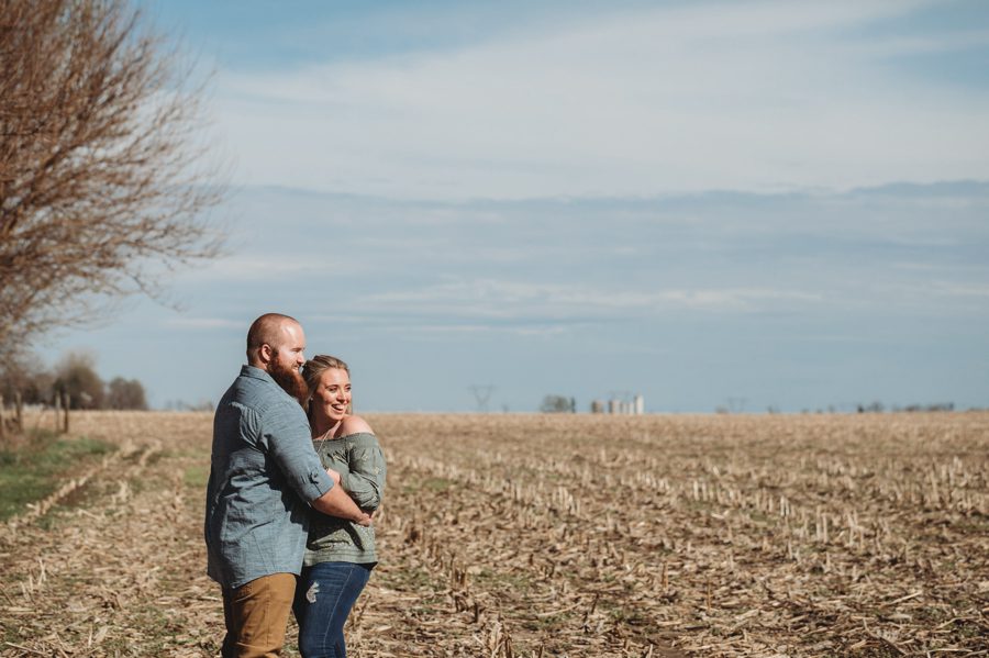 engaged couple cuddled together in field of private farm