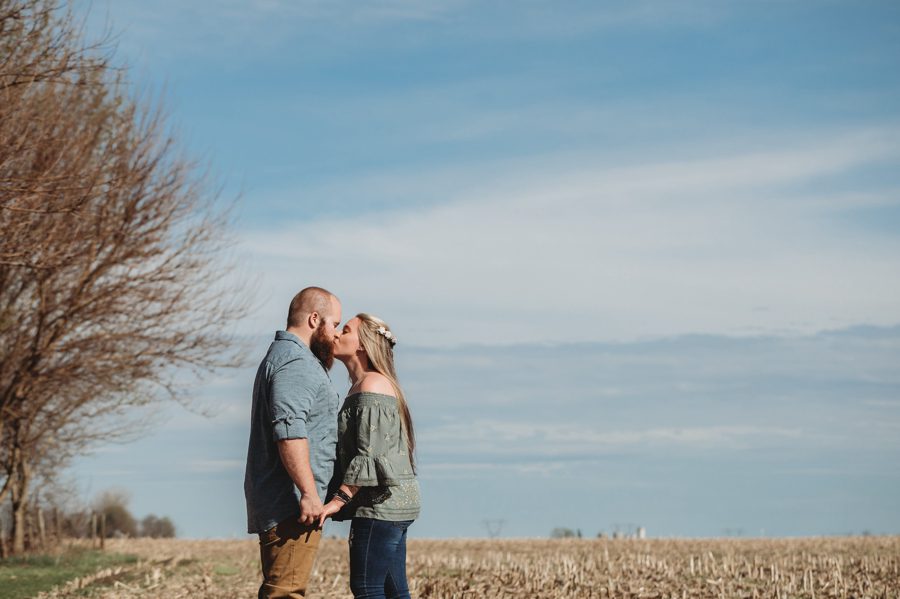 engaged couple standing in a field at a private farm kissing in full sun