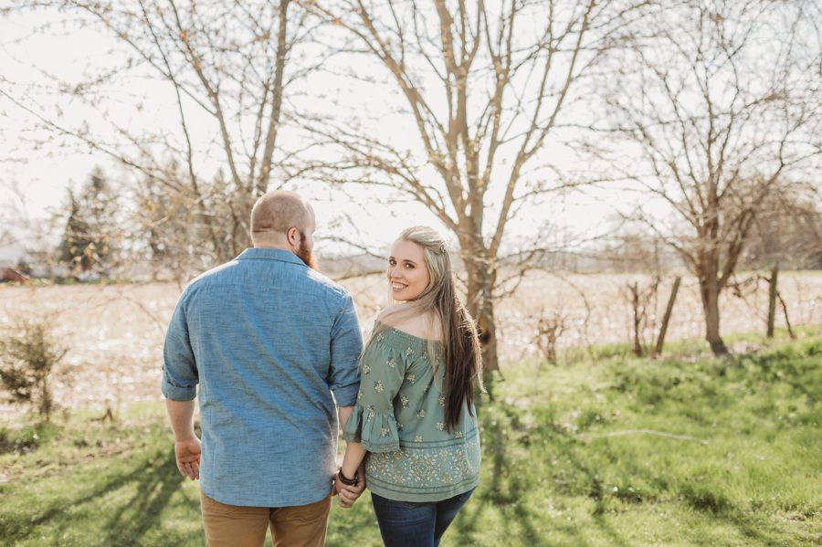 engaged couple walking with backs to photo and woman looking over shoulder