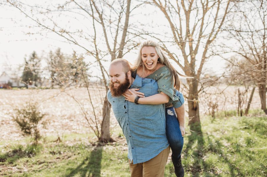 man in denim shirt and khaki pants giving fiancé a piggyback ride at Mt. Sterling Ohio Engagement Photos