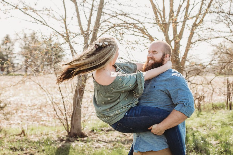 man in denim shirt swinging fiancé while holding her