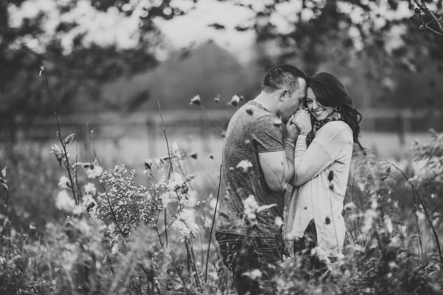 groom to be kissing fiancés hands in a field of milkweed