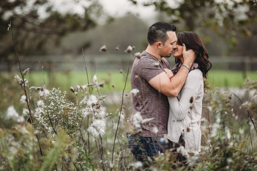 groom to be romantically kissing fiancé in milkweed field