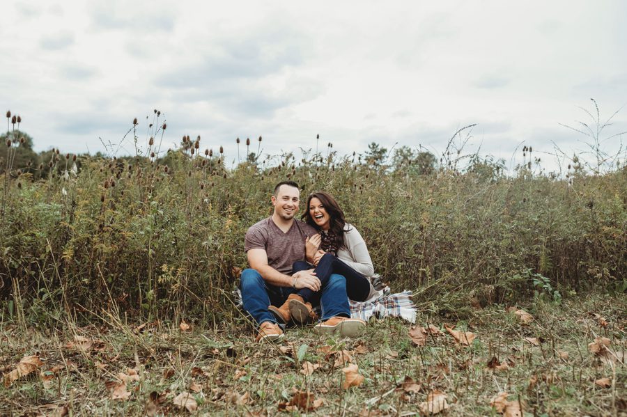 engaged couple sitting on plaid blanket in front of a field at Rotary Park in Newark Ohio