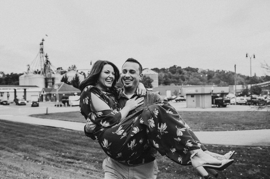 black and white image of groom to be carrying fiancé up a hill