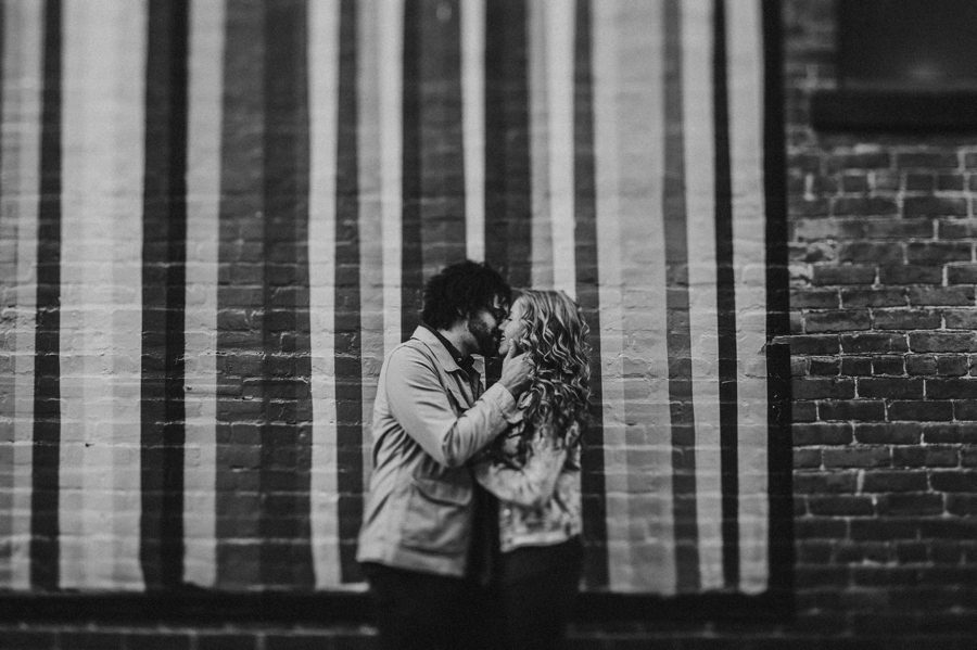 black and white image of engaged couple kissing in front of striped wall