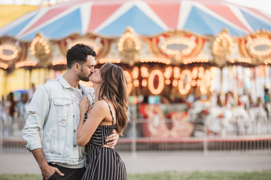 engaged couple kissing in front of carousel at Ohio State Fair