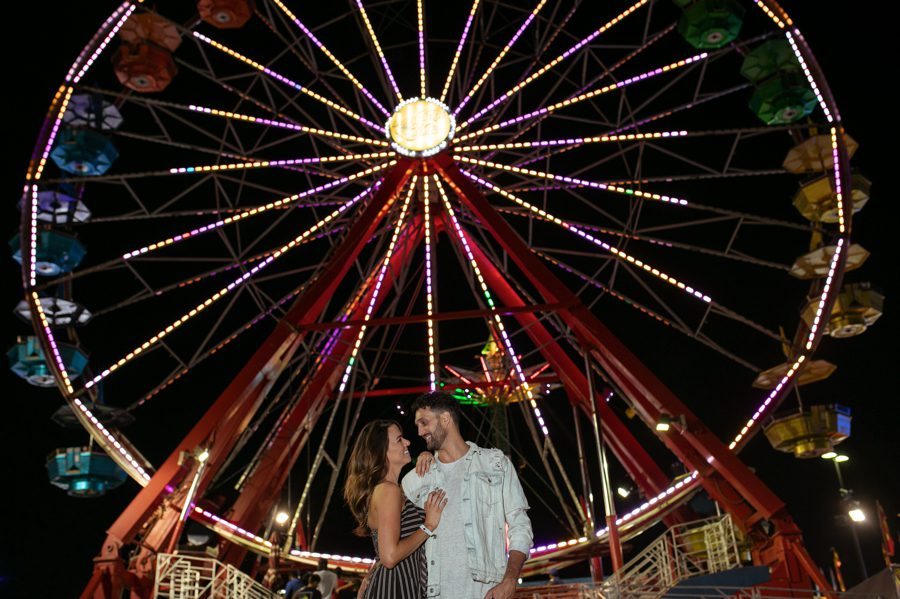 engaged couple looking at each other in front of ferris wheel at Ohio State Fair in Columbus