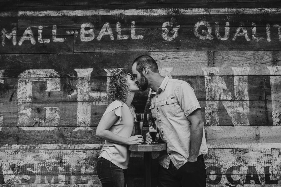 black and white image of engaged couple kissing in front of wood wall