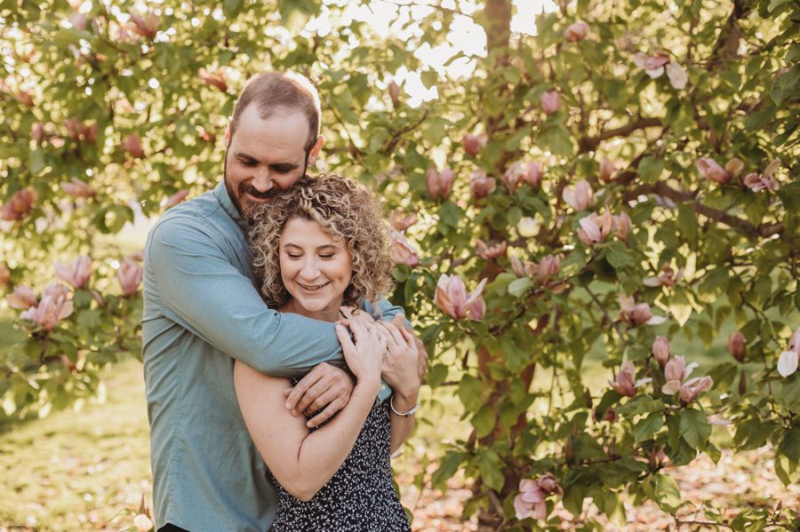 man hugging fiancé with magnolia trees in Columbus Ohio