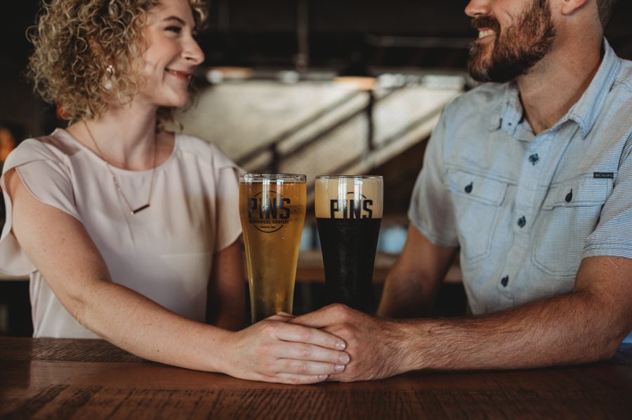 engaged couple looking at each other holding hands with beer