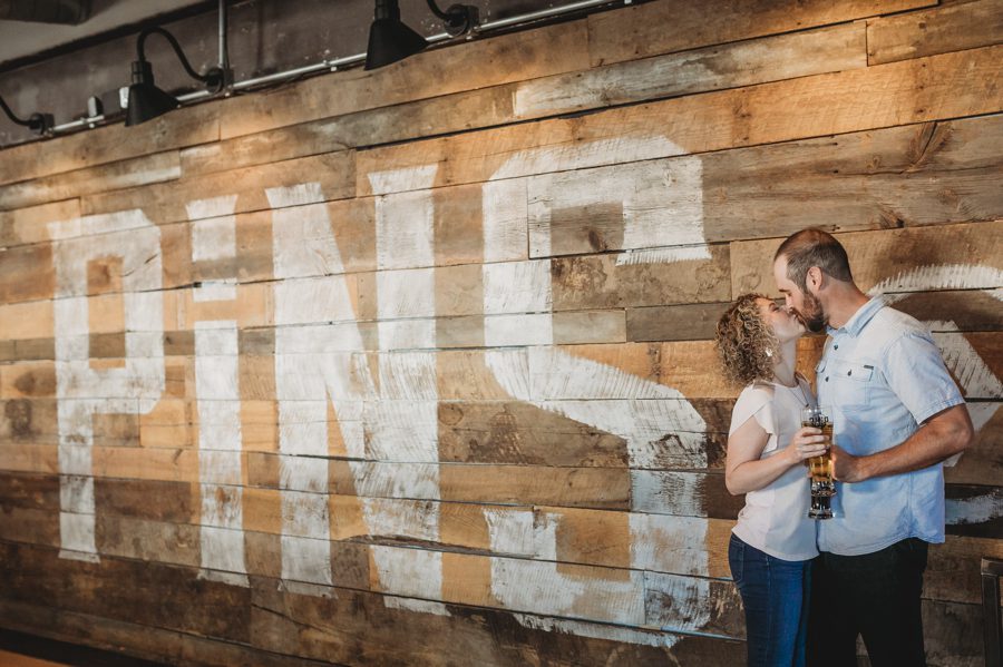 engaged couple kissing in front of wood wall at Pins Mechanical Engagement