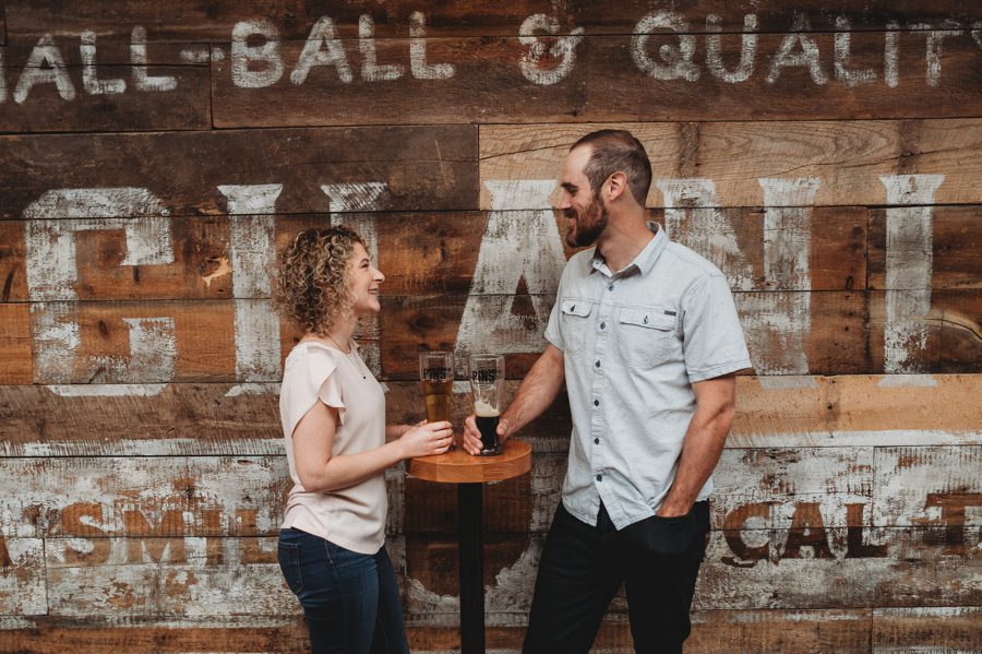 engaged couple looking at each other in front of wood wall