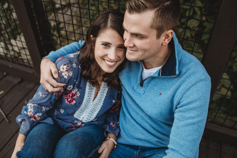 man in blue sweater with arm around fiancé and her smiling at camera