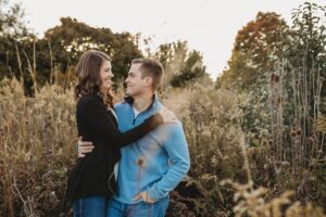 engaged couple looking at each other in a field with arms around each other