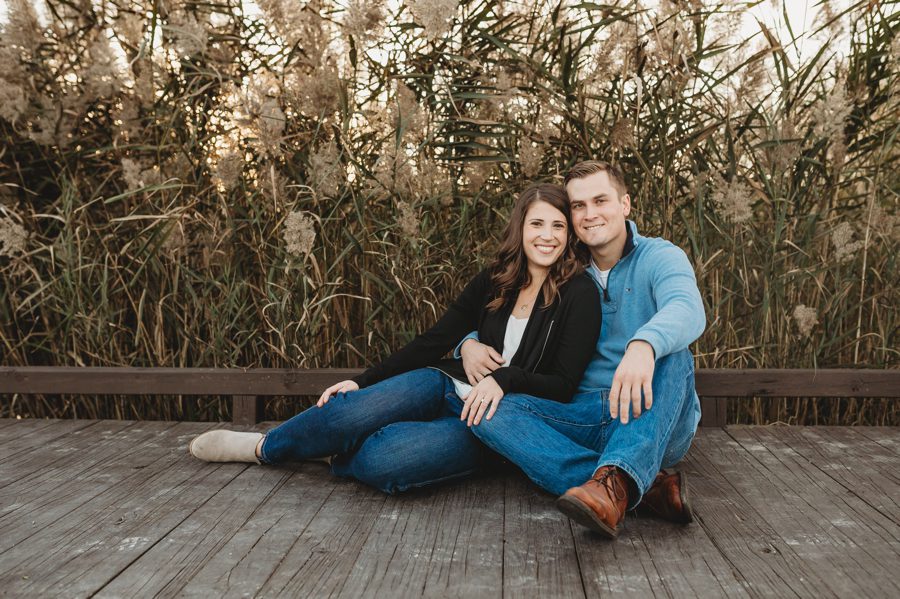 engaged couple sitting with each other with ornamental grass behind them