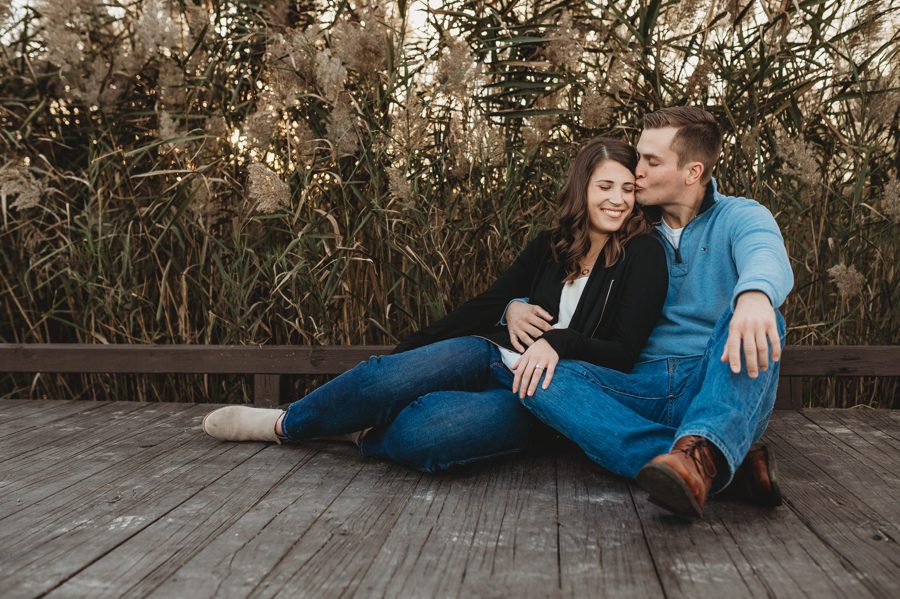 man in blue sweater kissing fiancés temple while sitting on ground