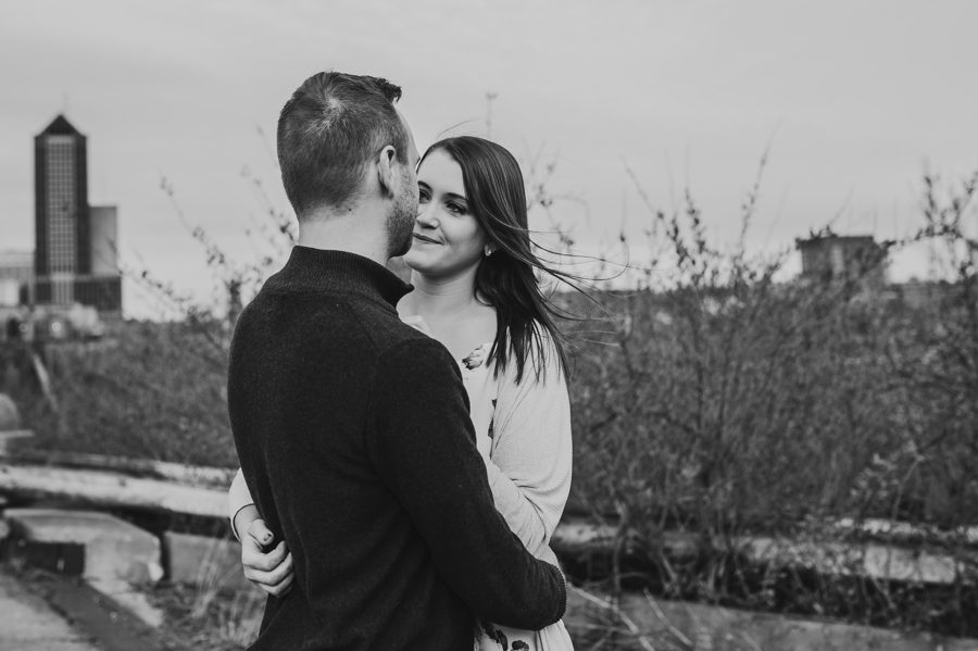 black and white image of man looking at fiancé and her hair blowing in the wind